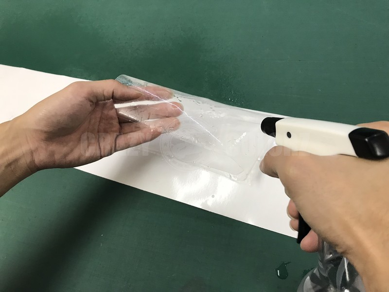 リアバンパープロテクションフィルム本体に水溶液を吹き付けて糊面を濡らしている様子