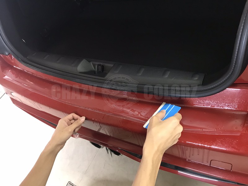 MINI Cooper Sのリアバンパープロテクションをスキージーで水抜きしながら貼り付けている様子